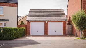 Un garage attenant à une maison, avec deux portes blanches, un toit en pente et une allée pavée.