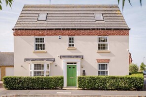 A two-story building with a green door, white-framed windows, and a brick base. - Spacious 5-bed Home in Milton Keynes by Renzo, Driveway Parking, Close to M1 (Milton Keynes)