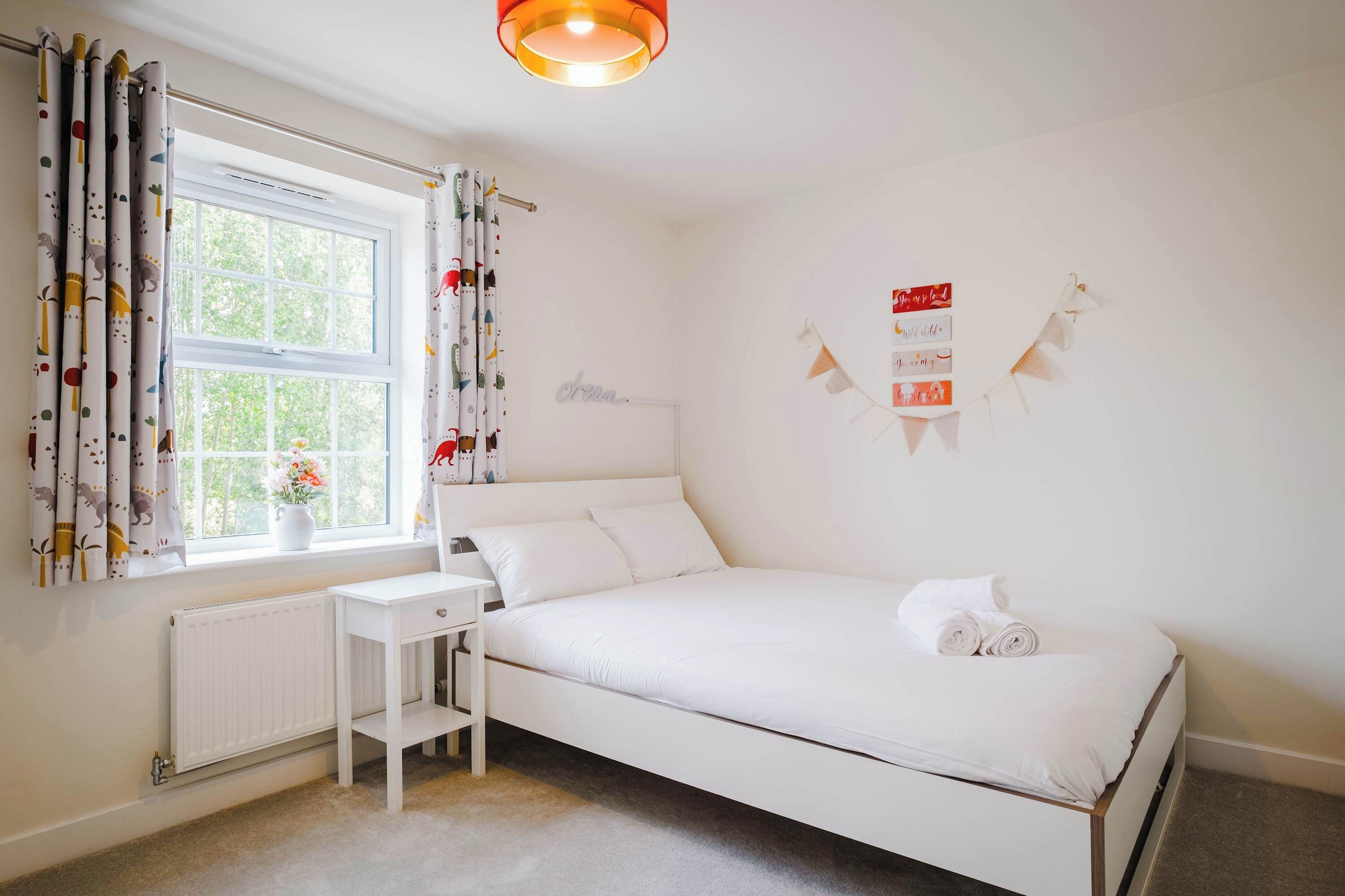Une chambre avec un lit simple, un bureau, un radiateur et une fenêtre avec des rideaux.