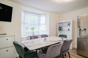 A modern kitchen with a marble countertop, a built-in fridge, and a dining area with a table and chairs. - Spacious 5-bed Home in Milton Keynes by Renzo, Driveway Parking, Close to M1 (Milton Keynes)