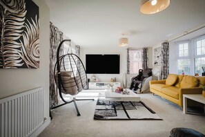 A modern living room with a hanging chair, a yellow sofa, a flat-screen TV, and a large window. - Spacious 5-bed Home in Milton Keynes by Renzo, Driveway Parking, Close to M1 (Milton Keynes)