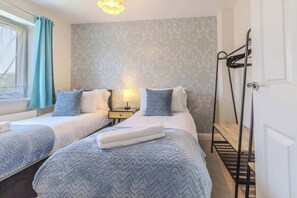 A hotel room with two beds, a nightstand, a lamp, a window with curtains, and a door with a towel rack. - Spacious and Cosy 3-bed Home in Bedford by Renzo, Free Parking, Close to A6 (Bedford)