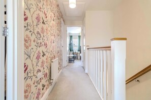 A hallway with floral wallpaper, a white radiator, and a wooden staircase railing.