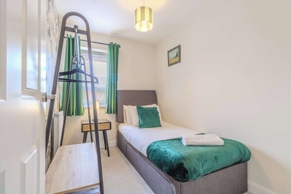 A bedroom with a bed, a bedside table, a hanging light fixture, and a window with curtains.