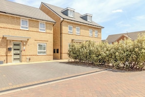 A two-story brick building with a flat roof, a small garden area, and a paved driveway.