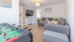 Ein Wohnzimmer mit einem Kicker, einem grauen Sofa und einem Fernseher an der Wand.
