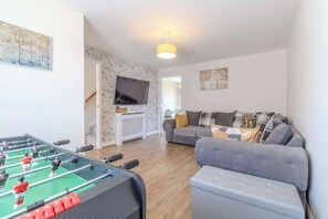 A living room with a foosball table, a grey sofa, and a television on the wall. - Spacious and Cosy 3-bed Home in Bedford by Renzo, Free Parking, Close to A6 (Bedford)