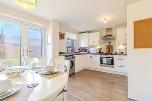 A modern kitchen with white cabinets, a built-in oven, microwave, and a washing machine. - Spacious and Cosy 3-bed Home in Bedford by Renzo, Free Parking, Close to A6 (Bedford)
