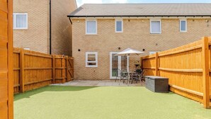 Ein Backsteinhaus mit einem umzäunten Hinterhof, einer Terrasse mit Gartenmöbeln und einem überdachten Sitzbereich.