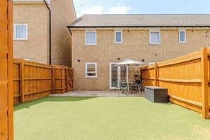 A brick building with a fenced backyard, a patio with outdoor furniture, and a covered seating area. - Spacious and Cosy 3-bed Home in Bedford by Renzo, Free Parking, Close to A6 (Bedford)