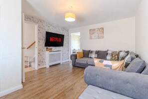 A living room with a grey sofa, a television mounted on a white stand, and a wooden floor.