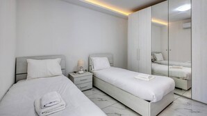 A modern bedroom with two beds, a nightstand, a mirror, and a wardrobe. - Bright Modern, fully equipped 3BR home w/AC & WIFI (Birkirkara)