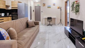 A modern living room with a sofa, a TV, a desk, and a chair. - Bright Modern, fully equipped 3BR home w/AC & WIFI (Birkirkara)