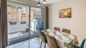 A dining area with a table set for four, a washing machine, and a view of the street through a large window. - Bright Modern, fully equipped 3BR home w/AC & WIFI (Birkirkara)
