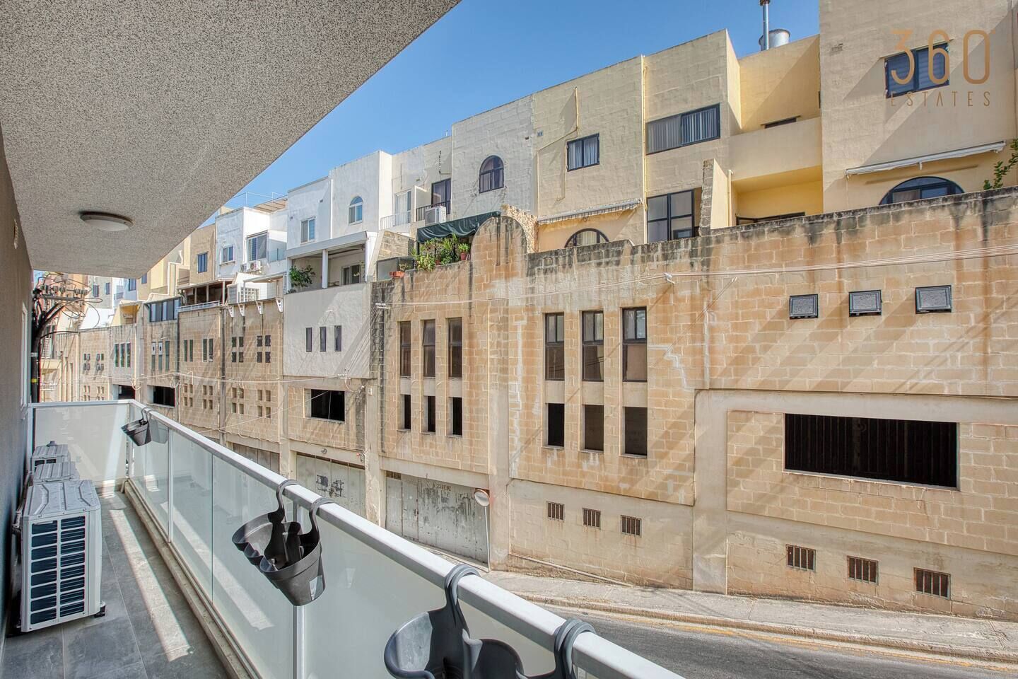 A balcony with a glass railing overlooking a row of buildings with multiple windows and balconies.