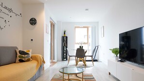 Una sala moderna con sofá, una mesa de centro de vidrio, televisor y una zona de comedor con sillas.