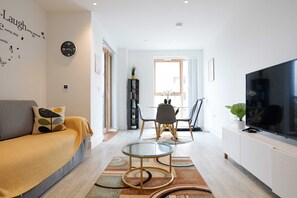 Una sala moderna con sofá, una mesa de centro de vidrio, televisor y una zona de comedor con sillas.