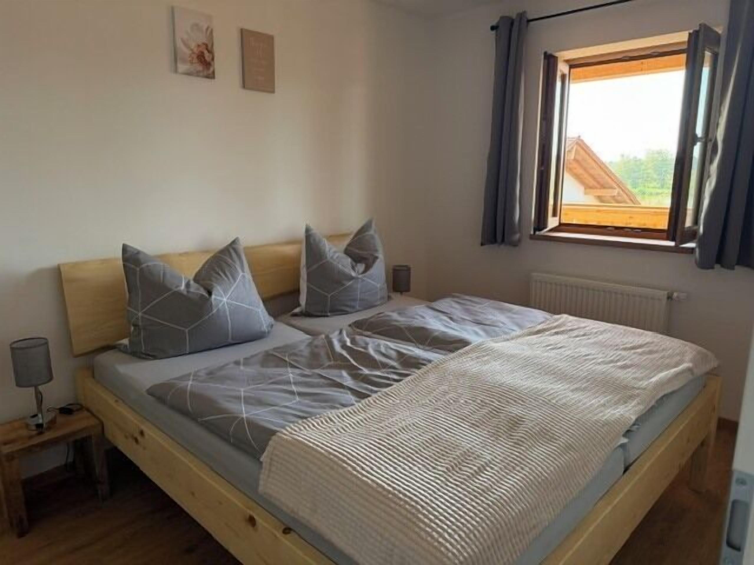 Un lit simple avec une tête de lit en bois, une literie grise et une fenêtre avec des rideaux.