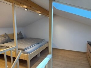 Une pièce aux hauts plafonds, avec un plafond en pente, un lit superposé et un puits de lumière.