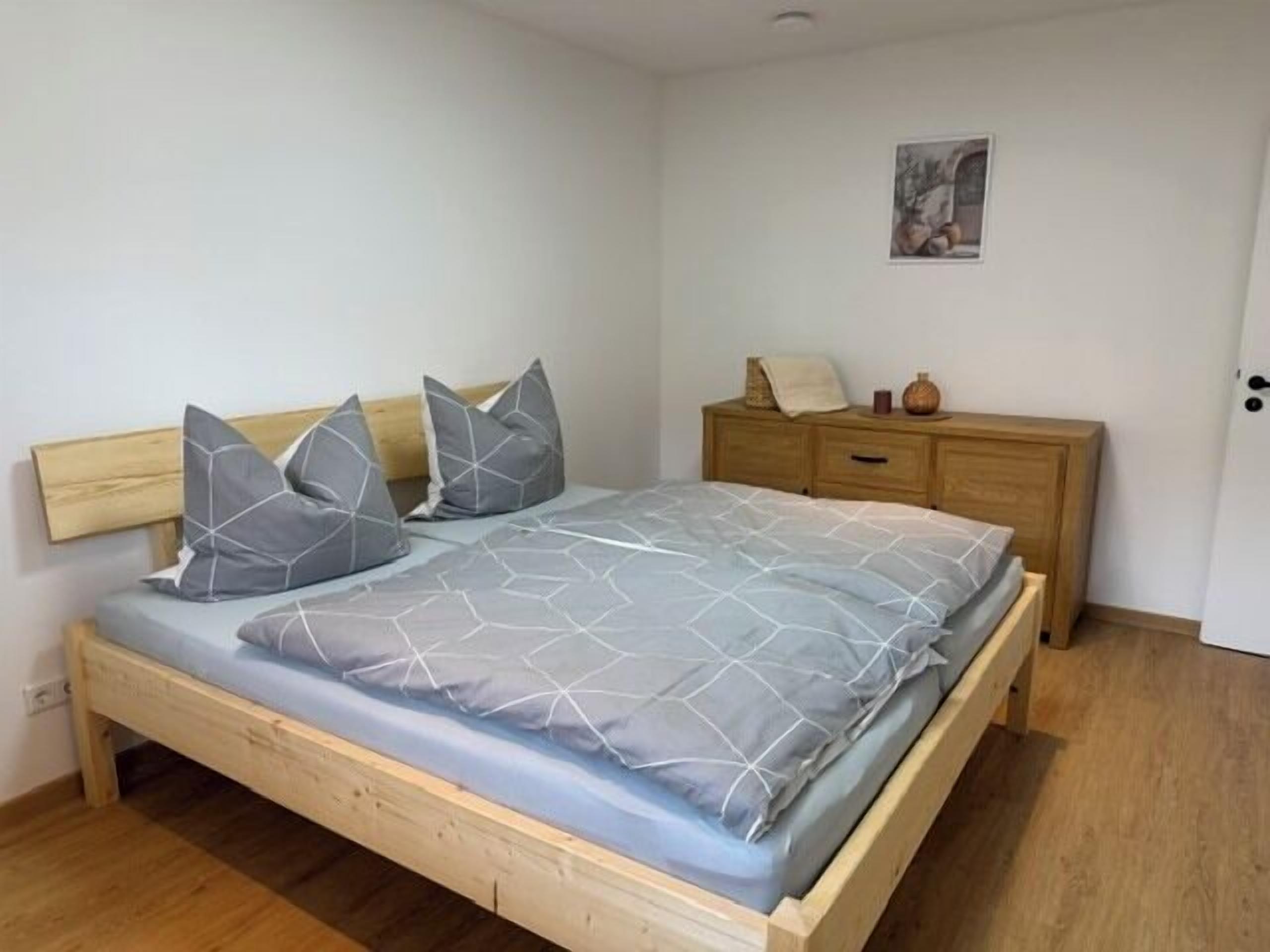 Une chambre à coucher avec un lit en bois, une literie grise, une table de chevet et une commode.