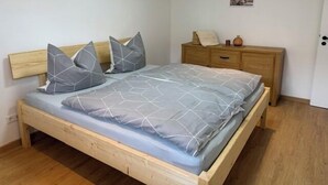 A bedroom with a wooden bed, grey bedding, a bedside table, and a dresser.