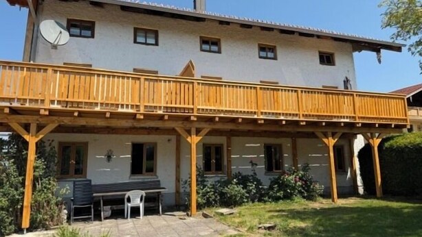 Ein zweistöckiges Gebäude mit einem Holzbalkon, einer Satellitenschüssel und einer Terrassenfläche mit Tisch und Stühlen.