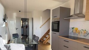 A modern kitchen with a glass dining table, grey cabinets, and a wooden staircase.