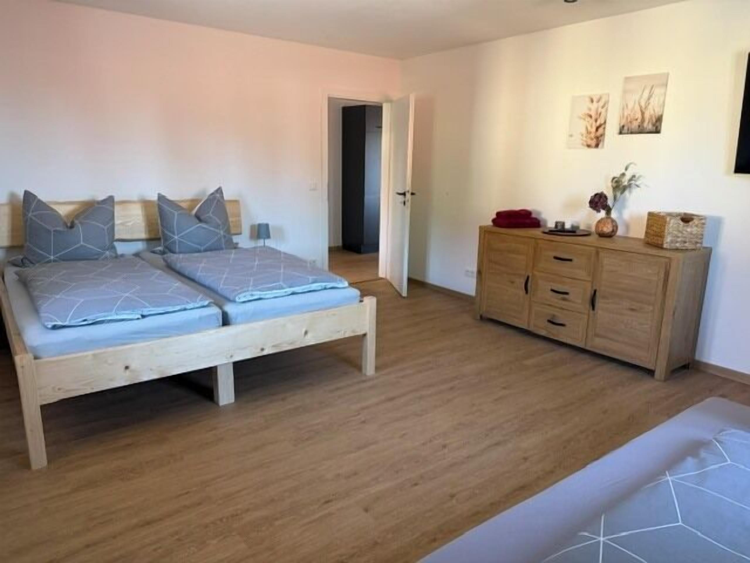 A bedroom with a wooden bed, a wooden dresser, and a door leading to another room.
