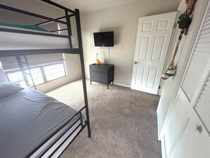 A bunk bed room with a television, a small cabinet, and a door. - 4BR Furnished Home in Waikoloa Village. Private Gym + Back Yard Entertainment (Waikoloa Village)