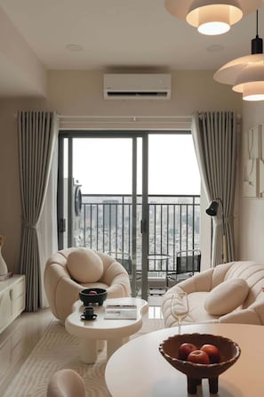 A modern living room with a sofa, armchair, and a dining table with a bowl of fruit. - Corner 2BR/3Beds • River View • Walk to Bui Vien (Thành phố Hồ Chí Minh)