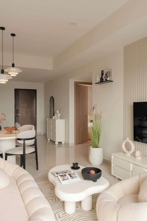 A modern living room with a sofa, a coffee table, a TV, and a dining area with chairs and a table. - Corner 2BR/3Beds • River View • Walk to Bui Vien (Thành phố Hồ Chí Minh)