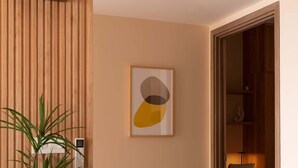 A modern interior with a wooden panel wall, a framed abstract artwork, a potted plant, and a white ottoman. - High-Rise | 2Br+1Wc | Central | D1 | 1min BuiVien (Thành phố Hồ Chí Minh)