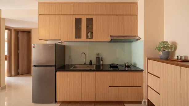 A modern kitchen with wooden cabinets, a stainless steel refrigerator, and a sink. - High-Rise | 2Br+1Wc | Central | D1 | 1min BuiVien (Thành phố Hồ Chí Minh)