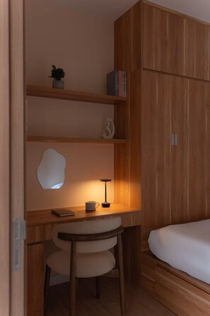 Ein gemütliches Schlafzimmer mit einem Holzschrank, einem Schreibtisch mit Stuhl, einem Nachttisch und einer kleinen Nachttischlampe.