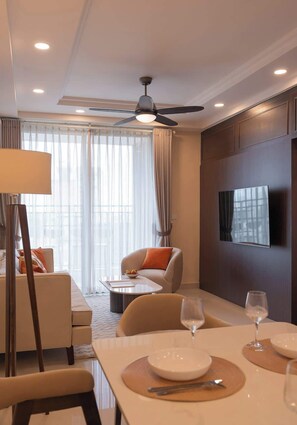 A hotel room with a dining area, a sofa, a television, and a ceiling fan. - 3BR+2BA | 4 Beds | Sleeps 11 | Bitexco View | D1 (Thành phố Hồ Chí Minh)