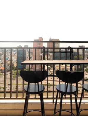 A balcony with two black chairs and a table, overlooking a cityscape with various buildings and a construction crane. - 3BR+2BA | 4 Beds | Sleeps 11 | Bitexco View | D1 (Thành phố Hồ Chí Minh)