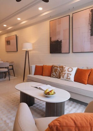 A modern living room with a sofa, a coffee table with a bowl of fruit, and a floor lamp. - 3BR+2BA | 4 Beds | Sleeps 11 | Bitexco View | D1 (Thành phố Hồ Chí Minh)