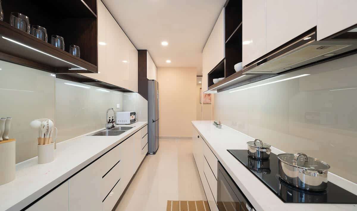 Une cuisine moderne avec des meubles blancs, une plaque de cuisson noire et un réfrigérateur en acier inoxydable.