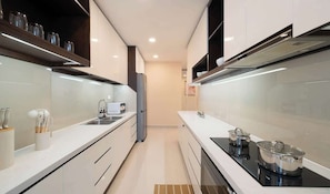 A modern kitchen with white cabinetry, a black stovetop, and a stainless steel refrigerator. - 3BR+2BA | 4 Beds | Sleeps 11 | Bitexco View | D1 (Thành phố Hồ Chí Minh)