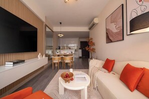 A modern living room with a sofa, a coffee table, and a TV. There is a dining area with a kitchen in the background. - Stay Together | 5BRs/4BA on Same Floor for Groups (Thành phố Hồ Chí Minh)
