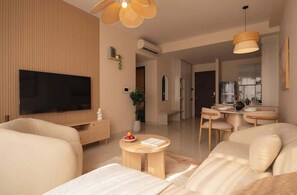 Ein modernes Wohnzimmer mit Fernseher, einem runden Couchtisch und einem Essbereich mit kleinem Tisch und Stühlen.