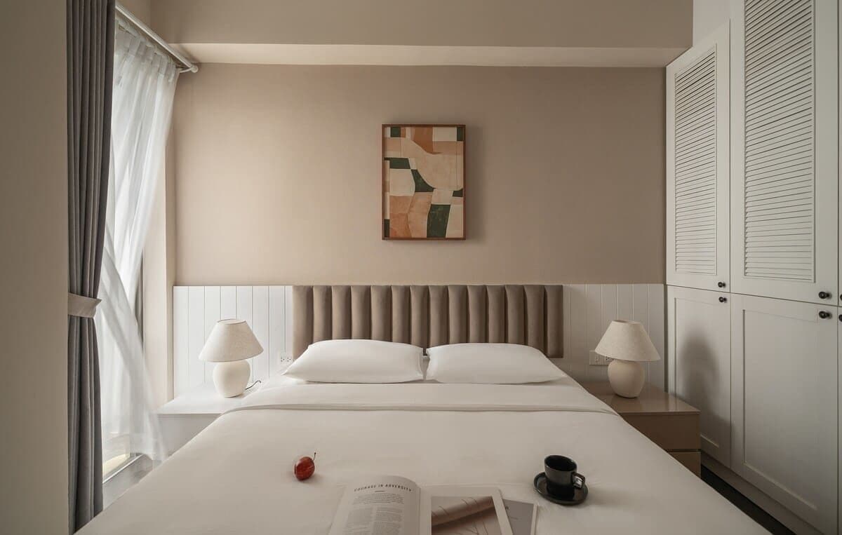 Ein Hotelzimmer mit Bett, Nachttischlampen, einem Bild an der Wand und einem Fenster mit Vorhängen.
