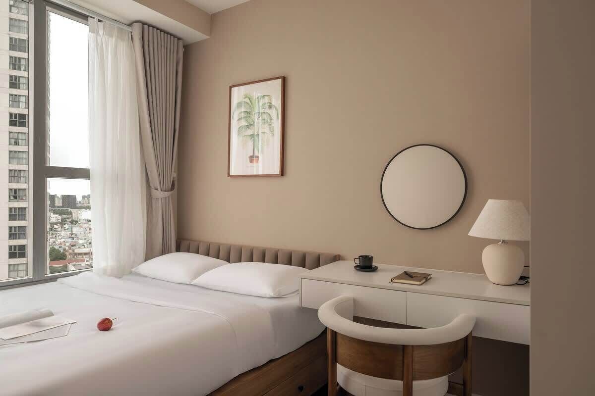 Habitación de hotel con cama, escritorio, silla, espejo redondo y un cuadro en la pared.