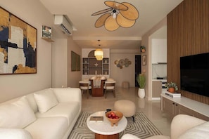 A modern living room with a sofa, a coffee table, a dining area with a table and chairs, and a television on a stand. - Minimalist Cozy 3BR/2BA • D1 Center• 200m Bui Vien (Thành phố Hồ Chí Minh)