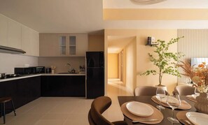 A modern kitchen with dark cabinetry, a black refrigerator, and a dining area with a table set for two. - Side by Side• 32nd Fl • 5BR | 7 Beds • Central D1 (Thành phố Hồ Chí Minh)