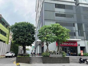 A modern building with a large tree in front, a sign for 'SOHO' and 'PHINDELI' on the ground floor, and a parked car. - Side by Side• 32nd Fl • 5BR | 7 Beds • Central D1 (Thành phố Hồ Chí Minh)