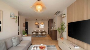 Un soggiorno moderno con un divano, un tavolino da caffè con riviste, una televisione e un'area da pranzo sullo sfondo.