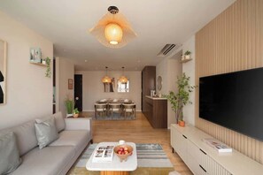 Ein modernes Wohnzimmer mit einer Couch, einem Couchtisch mit Zeitschriften, einem Fernseher und einem Essbereich im Hintergrund.