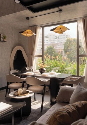 Ein modernes Interieur mit Essbereich, einer Couch und einem großen Fenster mit Blick auf Gebäude und Grünflächen.
