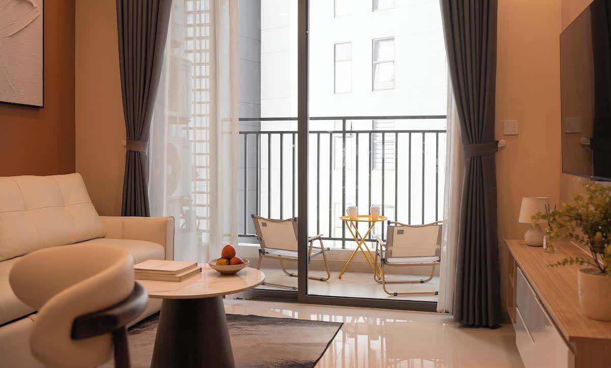 Una sala de estar moderna con sofá, una mesa de centro con un frutero, una zona de comedor con sillas y un balcón con barandilla.